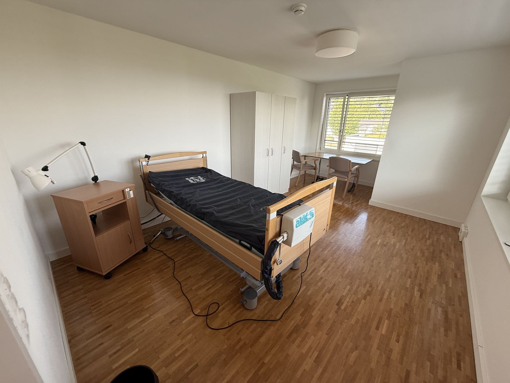 Eingerichtetes Zimmer mit Pflegebett, Schrank und Sitzecke
